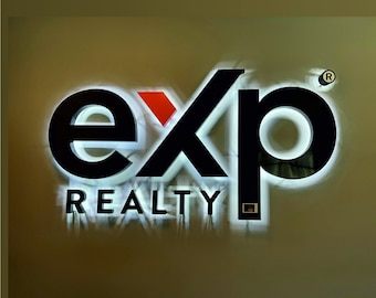 May include: A white sign with black lettering that reads "exp REALTY" with a red accent in the "x" and a registered trademark symbol in the upper right corner.