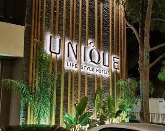 May include: A sign with the word "UNIQUE" in large, white letters on a black background. The sign is mounted on a wall with a wood and stone texture. The text "LIFE STYLE HOTELS" is below the word "UNIQUE".