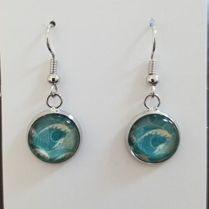 May include: A pair of silver dangle earrings with a blue and white wave design. The earrings are on a white card with the text "Maisie & Laurel Designs".