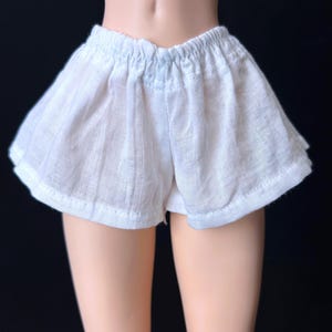 May include: White cotton shorts with a gathered elastic waistband. The shorts are made of a lightweight fabric and have a relaxed fit.