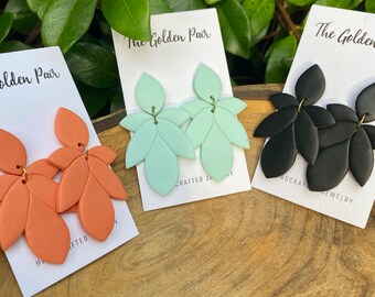 May include: Three pairs of handmade polymer clay earrings. The earrings are in the shape of leaves and are available in coral, mint green, and black.
