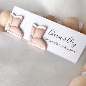 May include: A pair of pink and white boot-shaped earrings. The earrings are handmade in Wyoming by Charm & Clay.