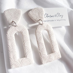 Peut inclure: Une paire de boucles d'oreilles en céramique blanche avec un motif en forme d'éventail. Les boucles d'oreilles sont faites à la main dans le Wyoming par Charm & Clay.