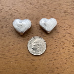 K&ouml;nnte beinhalten: Zwei silberne herzf&ouml;rmige Charms, jeder etwa so gro&szlig; wie eine Zehn-Cent-M&uuml;nze.