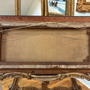 May include: The back of a wooden picture frame with a canvas stretched inside. The frame is dark brown with a wood grain pattern. The canvas is a light beige color and is attached to the frame with staples.