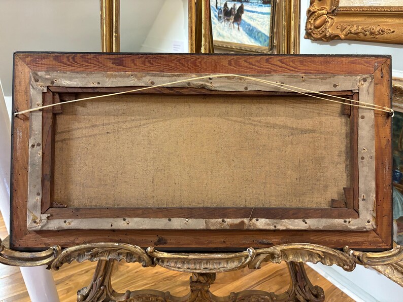 May include: The back of a wooden picture frame with a canvas stretched inside. The frame is dark brown with a wood grain pattern. The canvas is a light beige color and is attached to the frame with staples.