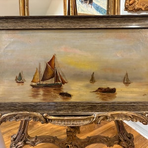 May include: A framed oil painting depicting a seascape with multiple sailboats on a calm body of water. The sky is a soft blue with hints of pink and yellow, suggesting a sunset or sunrise. The water is a warm brown color, reflecting the light of the sky.