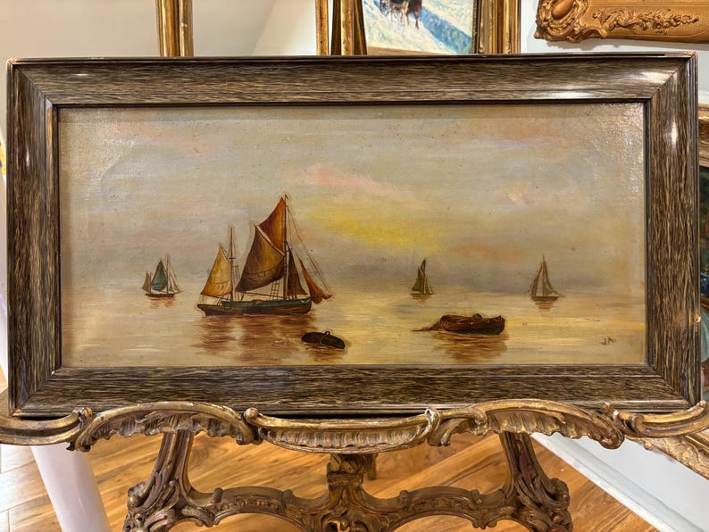 May include: A framed oil painting depicting a seascape with multiple sailboats on a calm body of water. The sky is a soft blue with hints of pink and yellow, suggesting a sunset or sunrise. The water is a warm brown color, reflecting the light of the sky.