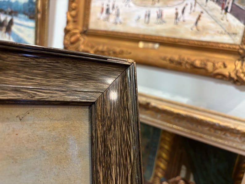 May include: Close-up of a dark brown wooden picture frame with a light brown canvas inside. The frame has a smooth, polished finish and a slightly raised edge.