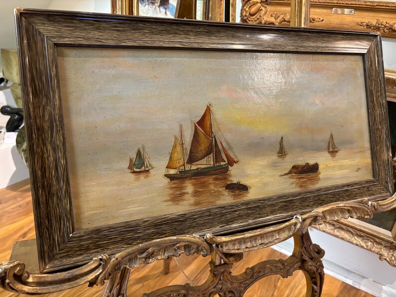 May include: A framed oil painting depicting a seascape with multiple sailboats on a calm body of water. The sky is a soft blue with hints of pink and yellow, and the water is a light blue with reflections of the boats. The painting is framed in a dark wood frame.