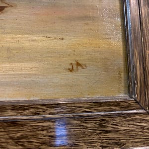 May include: A close-up of a framed painting with a light brown background and the initials "JA" in the lower right corner.