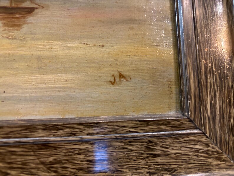 May include: A close-up of a framed painting with a light brown background and the initials "JA" in the lower right corner.