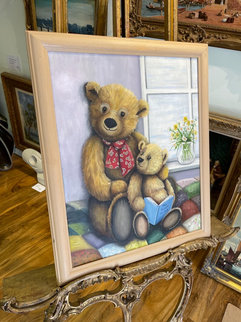 Puede incluir: Una pintura enmarcada de dos osos de peluche, uno con gafas y una bufanda roja, sentados en una colcha de retazos colorida. El oso m&aacute;s grande sostiene un oso m&aacute;s peque&ntilde;o y lee un libro titulado "The Very Busy Spider".