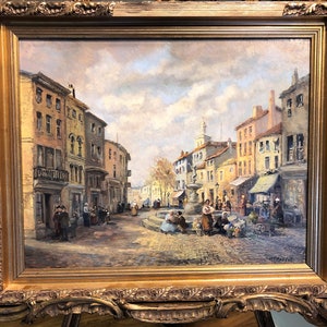 May include: A vintage oil painting depicting a bustling European street scene with buildings, a fountain, and people going about their day. The painting is framed in a gold ornate frame.