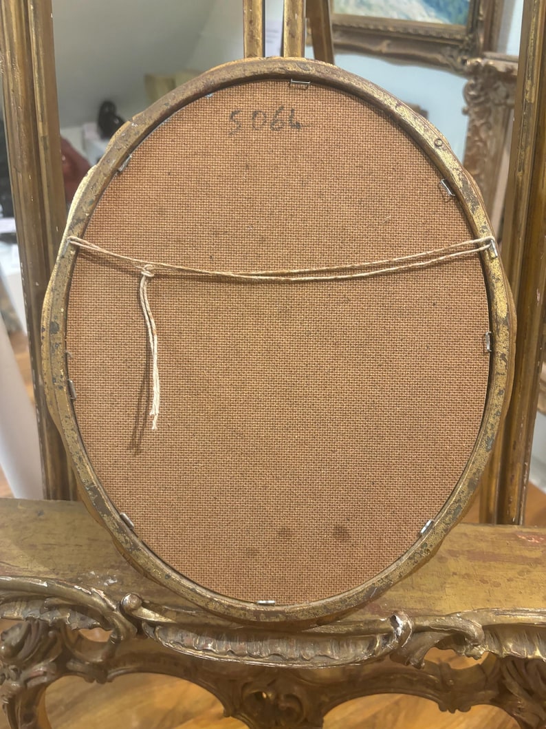 May include: The back of a gold oval picture frame with a brown fabric backing. The number "5066" is written on the back of the frame.