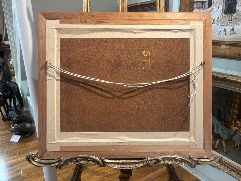 Puede incluir: La parte posterior de una pintura enmarcada con un marco de madera y un borde dorado. La parte posterior de la pintura est&aacute; hecha de cart&oacute;n marr&oacute;n. La pintura est&aacute; colgada en una pared.