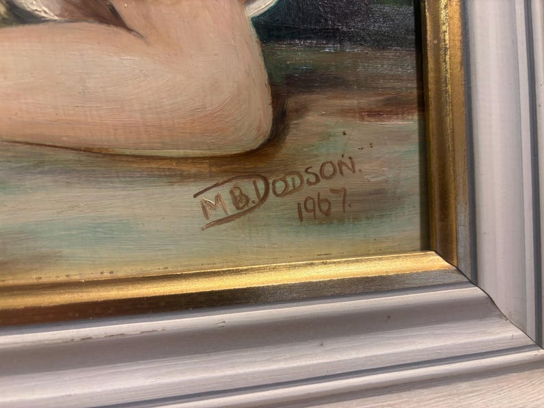 Puede incluir: Primer plano de una pintura con marco dorado. La pintura est&aacute; firmada "M.B. Dodson" y fechada "1967".