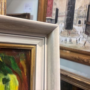 Puede incluir: Una pintura enmarcada con un marco blanco y dorado. La pintura representa una naturaleza muerta con una fruta verde y amarilla y un fondo marr&oacute;n.