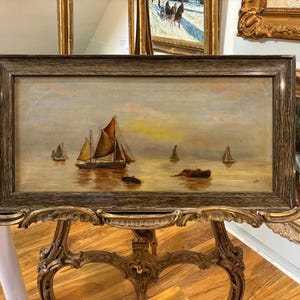 May include: A framed oil painting depicting a seascape with three sailboats in the distance. The sky is a soft blue with hints of pink and yellow. The water is a calm, golden brown.