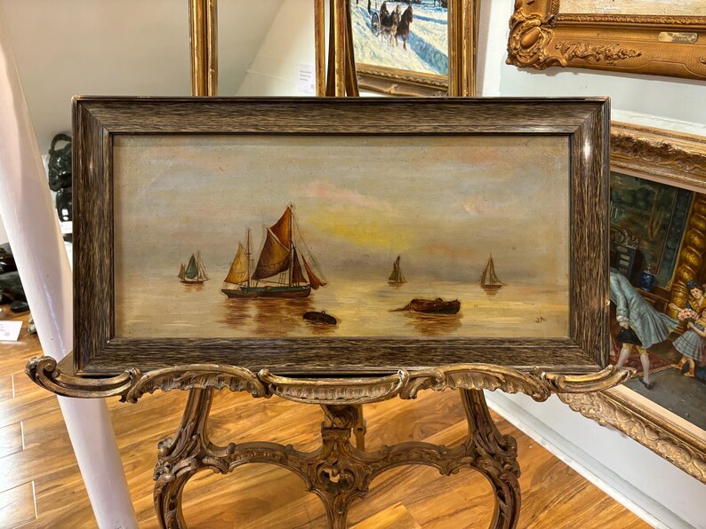 May include: A framed oil painting depicting a seascape with three sailboats in the distance. The sky is a soft blue with hints of pink and yellow. The water is a calm, golden brown.