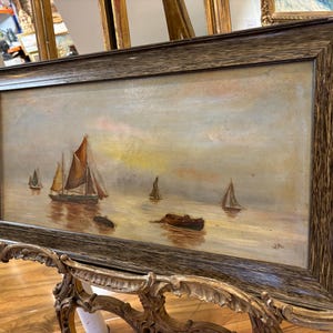 May include: A framed oil painting depicting a seascape with several sailboats on a calm body of water. The sky is a soft blue with hints of pink and yellow. The painting is in a dark wood frame.
