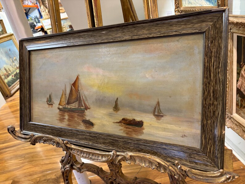 May include: A framed oil painting depicting a seascape with several sailboats on a calm body of water. The sky is a soft blue with hints of pink and yellow. The painting is in a dark wood frame.