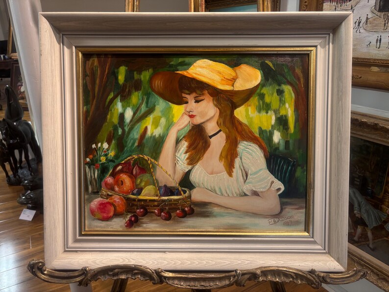 Puede incluir: Una pintura de una mujer con un sombrero de paja amarillo y un vestido blanco, sentada en un jard&iacute;n con una cesta de fruta delante de ella.