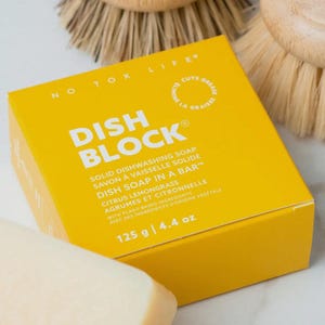 May include: A bright yellow square box of No Tox Life dish block solid dishwashing soap. The packaging features white text reading Dish Block, Dish Soap In A Bar, Citrus Lemongrass, and 125 g | 4.4 oz, with a circular logo stating Cuts Grease.