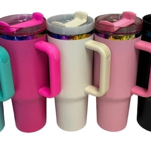 May include: A row of insulated tumblers in various colors: teal, pink, white, light pink, and black. Each tumbler has a matching handle and lid, with a metallic iridescent band near the top. The tumblers are designed to keep beverages cold or hot.