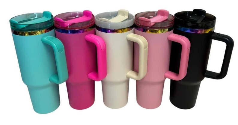 May include: Five stainless steel travel mugs with handles. The mugs are in various colors: teal, pink, white, light pink, and black. Each mug has a lid with a rainbow iridescent band.