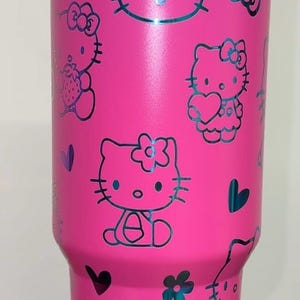 May include: Pink stainless steel tumbler with a black Hello Kitty design. The tumbler features multiple Hello Kitty characters with hearts and flowers.