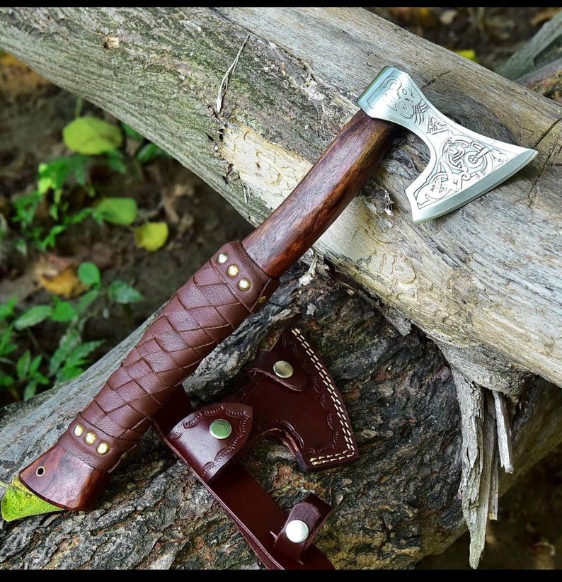 Puede incluir: Un hacha artesanal con mango de madera y hoja plateada con dise&ntilde;os intrincados. El mango est&aacute; envuelto en cuero marr&oacute;n con remaches de lat&oacute;n. Incluye una funda de cuero a juego.