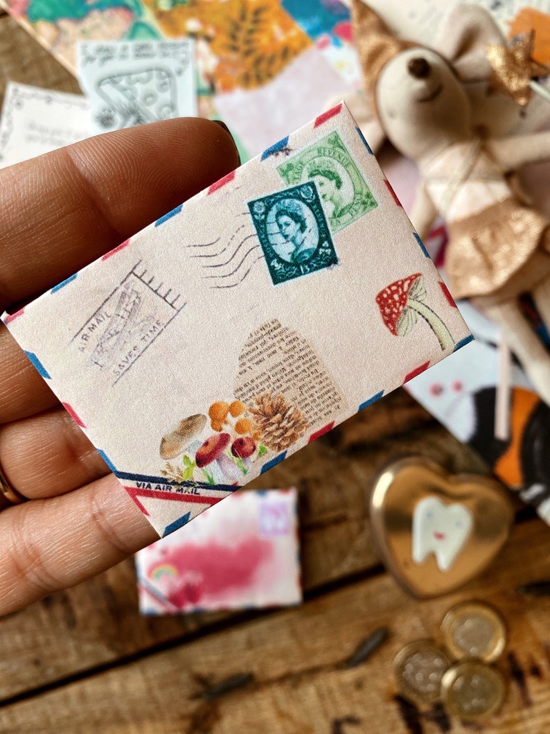 May include: A vintage-style envelope with a red, white, and blue border. The envelope has a postage stamp with a portrait of a woman and the words "Via Air Mail" printed on the bottom. The envelope is decorated with a mushroom and pine cone illustration.