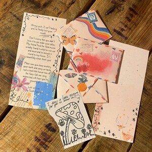 May include: A collection of colorful envelopes with handwritten notes and drawings. The envelopes feature rainbows, hearts, stars, and a deer. One note says "I drew a little picture for you to color in!!!" and includes a drawing of a mushroom.