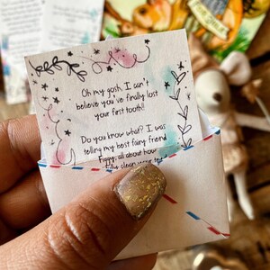 Puede incluir: Un peque&ntilde;o sobre blanco con una nota escrita a mano en su interior. La nota dice "Oh my gosh, I can't believe you've finally lost your first tooth!! Do you know what? I was telling my best fairy friend Figgy, all about how..." El sobre est&aacute; decorado con estrellas y un dise&ntilde;o floral.