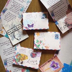 Puede incluir: Una colecci&oacute;n de sobres coloridos con notas escritas a mano e ilustraciones. Los sobres est&aacute;n decorados con flores, mariposas y otros dise&ntilde;os caprichosos. Las notas est&aacute;n dirigidas a "Luna" e incluyen mensajes del Hada de los Dientes.