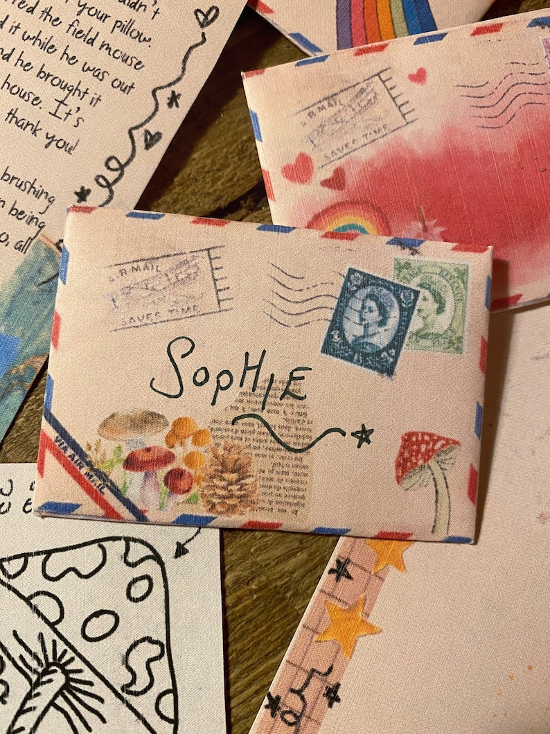 May include: A vintage-style envelope with a red, white, and blue border. The envelope has a stamp that says "IR MAIL SAVES TIME" and a stamp with a portrait of a woman. The envelope is addressed to "Sophie" and has a small star drawn on it.