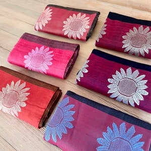 以下が含まれることがあります： ひまわり柄の生地見本が6種類あります。見本は赤、茶色、黒の様々な色合いです。ひまわりは銀、白、青の糸で刺繍されています。