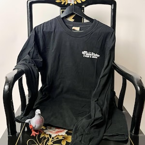 May include: A black long-sleeve t-shirt featuring a white graphic on the upper left chest that reads Fiddlesticks PUB & GRILL. The shirt has a crew neckline and is displayed on a black hanger. The fabric is solid black with long sleeves.