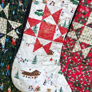 Könnte beinhalten: Drei gesteppte Weihnachtsstrümpfe mit festlichen Mustern. Der linke ist dunkelgrün mit Nussknackern, der mittlere ist cremefarben mit einem roten Stern und Winterszenen, und der rechte ist rot mit weißer Mistel und einem weißen Sternmuster.