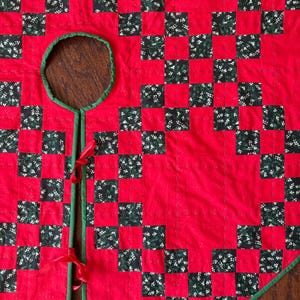 May include: Red and green checkered Christmas tree skirt with a green trim and a hole in the center for the tree trunk. The skirt is tied with red ribbons.