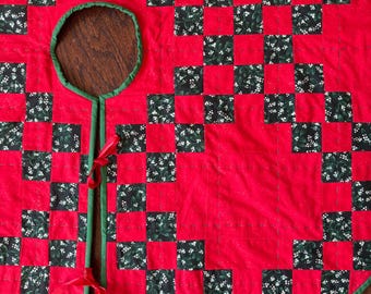 May include: Red and green checkered Christmas tree skirt with a green trim and a hole in the center for the tree trunk. The skirt is tied with red ribbons.