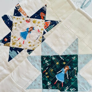 Könnte beinhalten: Zwei gesteppte Stoffsterne auf weißem Hintergrund. Der obere Stern ist blau mit goldenen Sternen und einem Mädchen in einem blauen Kleid. Der untere Stern ist grün mit weißen Sternen und einem Mädchen in einem blauen Kleid.