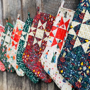 Pode incluir: Uma fila de oito meias de Natal feitas à mão com um padrão de colcha de estrela. As meias são feitas de vários tecidos com diferentes cores e padrões, incluindo vermelho, verde, azul, branco e dourado.