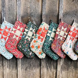 May include: Ten handmade Christmas stockings with a patchwork design. Each stocking features a different fabric with a star pattern in the center. The stockings are hung on a wooden wall.