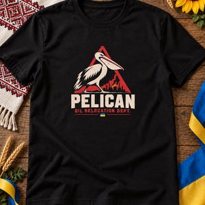 May include: A black short-sleeved t-shirt featuring a graphic of a pelican standing in front of a red triangle with a silhouette of an oil refinery. The text reads PELICAN OIL RELOCATION DEPT. with a small blue and yellow flag icon below it.