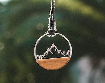 May include: A silver necklace with a round pendant featuring a wood-toned mountain scene.