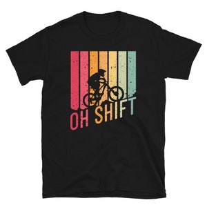 Könnte beinhalten: Schwarzes T-Shirt mit einer Retro-Grafik eines Mountainbikers, der einen Berg hinunterfährt, mit dem Text "OH SHIFT" in einer bunten Schrift.