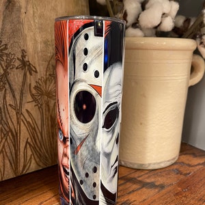May include: A stainless steel tumbler featuring a collage of horror movie characters. The design includes Chucky, Jason Voorhees, and Michael Myers. The tumbler has a black lid and a glossy finish, perfect for cold beverages.