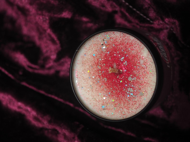 May include: A white candle with red glitter and a black wick in a black glass jar.
